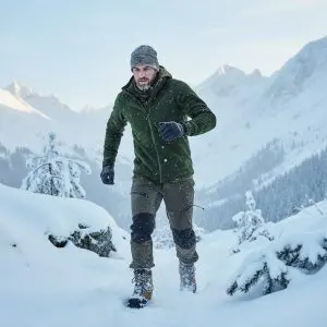 Homme en Tenue hivernale outdoor: veste verte épaisse, pantalons cargo et bottes de randonnée dans un paysage de montagne enneigée. Homme en Tenue hivernale outdoor: veste verte épaisse, pantalons cargo et bottes de randonnée dans un paysage de montagne enneigée.